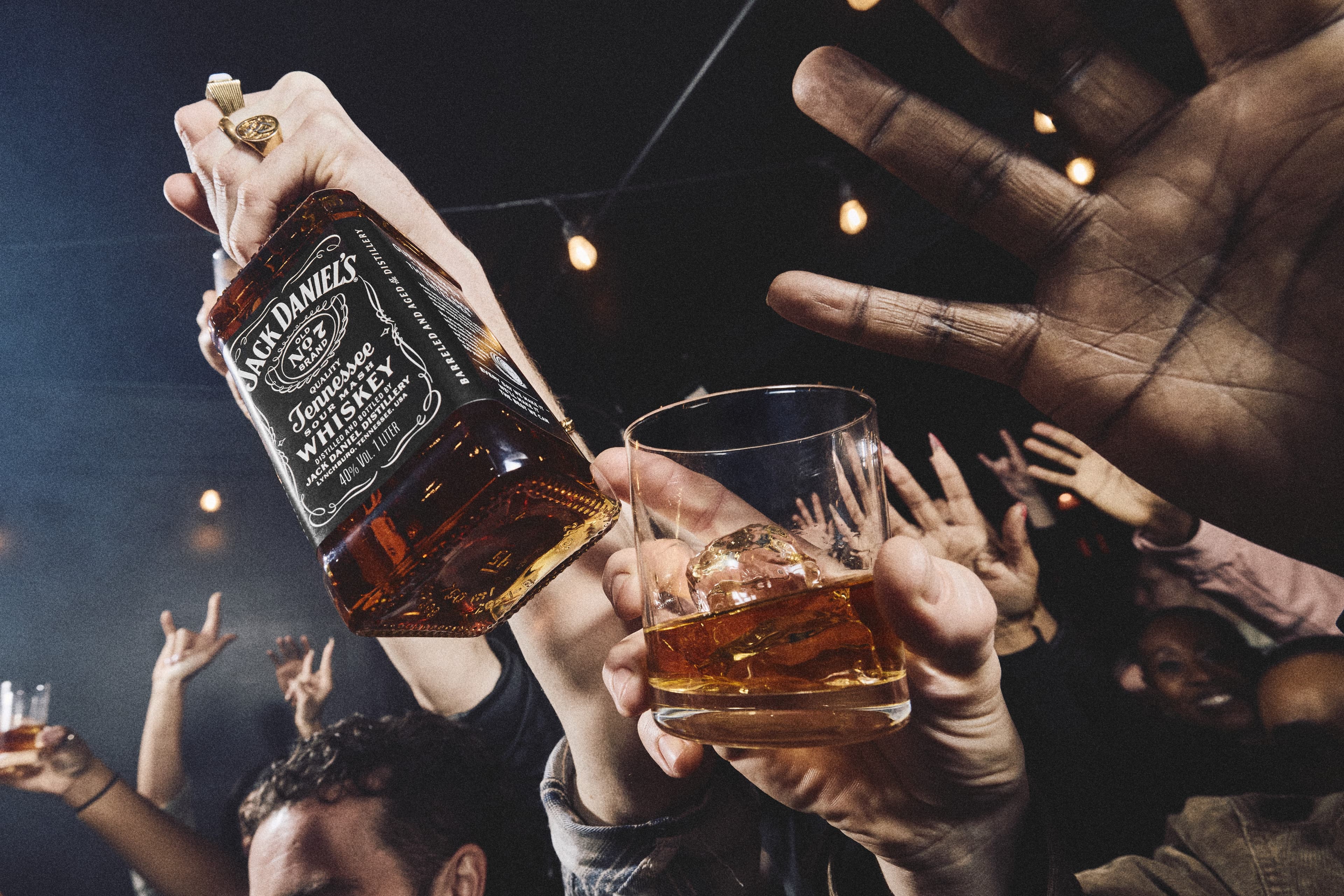 A person holding the neck of a bottle of Jack Daniel's in a crowd.